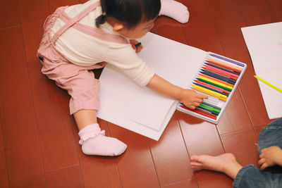 High angle view of girl drawing with crayons while sitting by brother at home