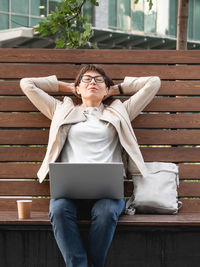 Freelance business woman sits in park with laptop and take away cup of coffee. working remotely.