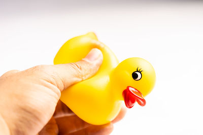 Close-up of hand holding yellow toy against white background