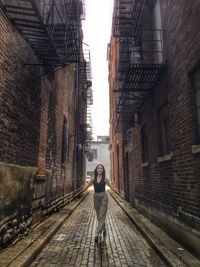 Portrait of mid adult woman with arms outstretched standing at alley amidst buildings