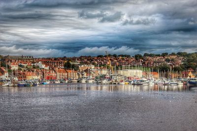 Boats at harbor against cloudy sky