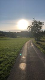 Road amidst field against sky during sunset