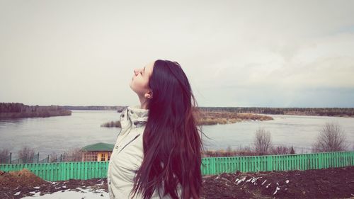 Side view of woman standing by water against sky