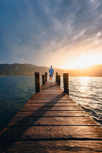 Young man on a wooden jetty on lake orta as he watches the sun set behind the mountains at sunset