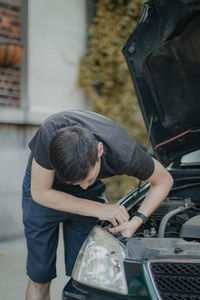 A young man unscrews a headlight bulb inside the hood.