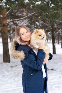 Young woman carrying dog while standing in snow during winter