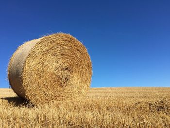 Hay bales on field against clear blue sky