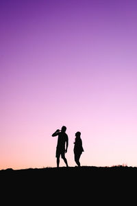 Silhouette friends standing on field against sky during sunset