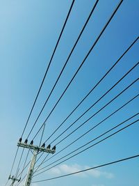 Low angle view of electricity pylon against clear blue sky