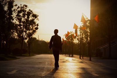 Rear view of silhouette man walking on street at sunset