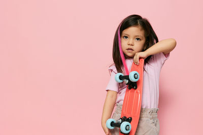 Portrait of cute girl with arms raised standing against pink background