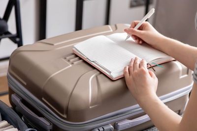 Cropped hand of woman writing in diary on suitcase