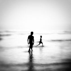 Silhouette father with son enjoying at beach against clear sky