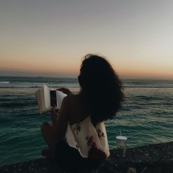 Woman at beach against sky during sunset