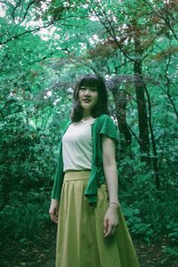 Portrait of woman standing by tree in forest