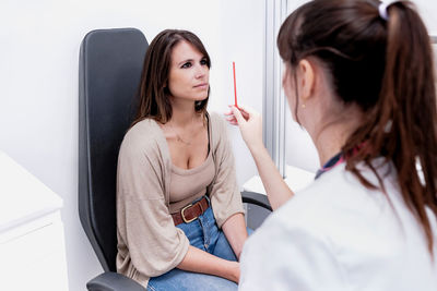 Unrecognizable female ophthalmologist using stick and checking vision of woman during appointment in modern clinic