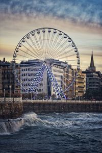 Ferris wheel in city against sky during sunset