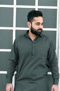 Bearded young man looking away while standing against wall