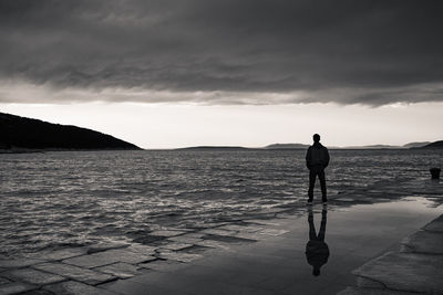 Rear view of man standing at beach against sky
