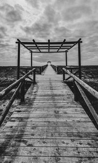 Wooden jetty leading to pier over sea against sky