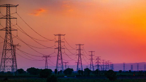 Silhouette electricity pylon on field against romantic sky at sunset