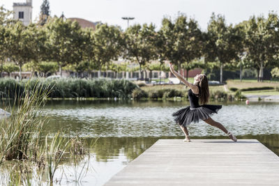 Woman ballet dancing on pier over lake against sky