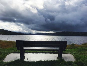 Empty bench by lake against sky