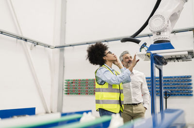 Engineer examining robotic arm machine standing by businessman in factory