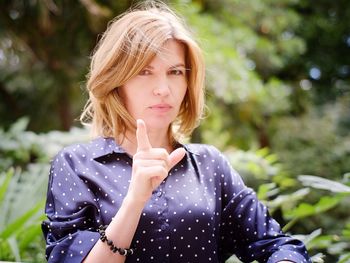 Portrait of woman pointing while standing against trees