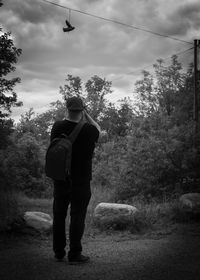 Rear view of man standing by trees against sky