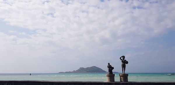 Statues by sea against sky