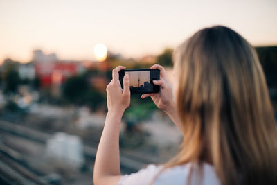 Young woman photographing fernsehturm through smart phone during sunset