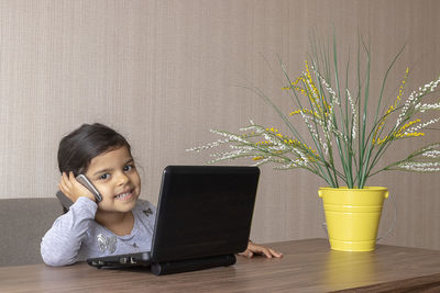 Cute girl using phone while sitting on table at home