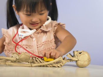 Close-up of girl examining skeleton with toy stethoscope at table