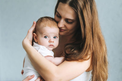 Portrait of young woman mom with long hair holding baby girl on hands at home