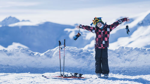 Portrait of happy boy with arms outstretched standing against snowcapped mountains