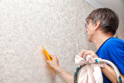 Mature painter using scrapper on wall