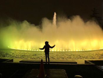 Silhouette child standing on fountain against yellow light