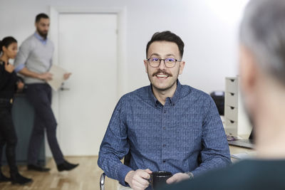 Smiling businessman holding coffee cup while discussing with professional at office