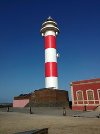 Low angle view of lighthouse against building against clear blue sky