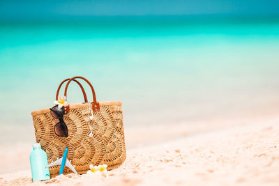 Wicker basket on sand at beach against blue sky
