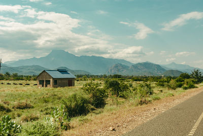 House on road by mountains against sky