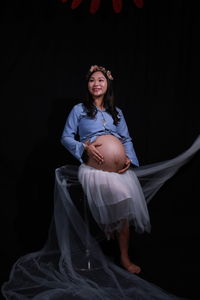 Full length of woman sitting against black background