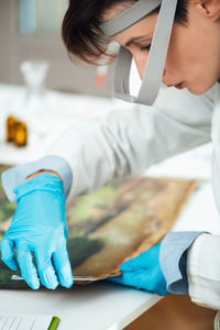 Female conservator with magnifying goggles cleaning dirt from antique oil painting