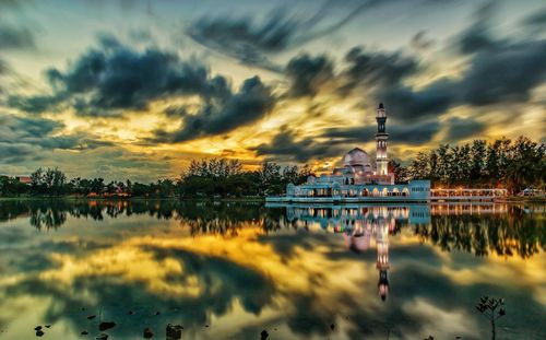 Scenic view of lake and floating mosque buildings against sky during sunset