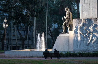 Statue of man sitting on bench in park