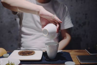 Midsection of man pouring drink in cup on table at restaurant