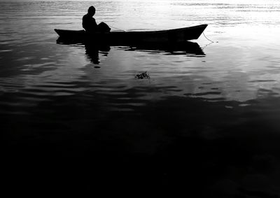 Silhouette man in boat on lake against sky