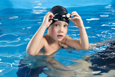 Preschool boy learning how to swim in a pool wearing swimming cap and goggles