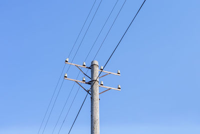 Low angle view of electricity pylon against clear blue sky